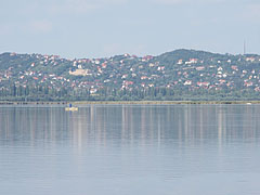 An angler in his boat on the Velence Lake, and the houses of Sukoró village on the hillside - Agárd, Maďarsko