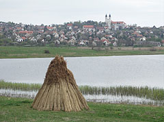 Bundles of reeds in front of the Inner Lake ("Belső-tó"), and behind it in the distance there are the houses of the village, as well as the double towers of the Benedictine Abbey Church - Tihany, Macaristan