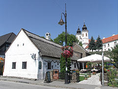 The Csárdás Restaurant in the farmhouse with porch, and some distance away there are the white steeples (towers) of the Benedictine Abbey of Tihany - Tihany, Ungarn