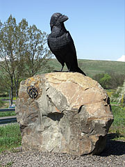 Iron statue of a black bird (a raven) on a rock at the crossroads, with the logo of the UNESCO World Heritage Site - Hollókő, Macaristan