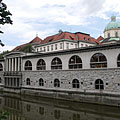 The so-called Plečnik's arcades building complex by the river, and some distance away the roof of the covered market hall ("Pokrita tržnica") and the dome of the Cathedral of St. Nicholas can be seen - Ljubljana, Slovenia