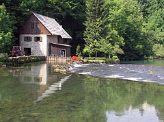 A stone house with a wooden water mill building on its side by the Slunjčica River (also known by the locals as Slušnica), opposite the hill with the castle ruins - Slunj, Croazia