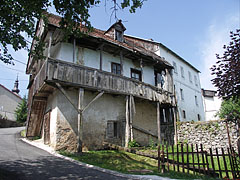 An old crumbling two-storey house on the steep winding street, with a timer porch on upstairs - Slunj, Croazia