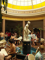 Statue of a bathing woman on a fountain in the dome hall of the bath, surrounded by restaurant tables - Miskolc, Hongarije